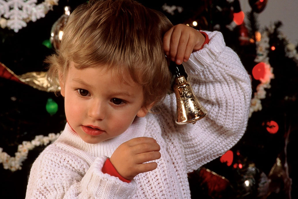 Kind mit Weihnachtglocke vor Christbaum